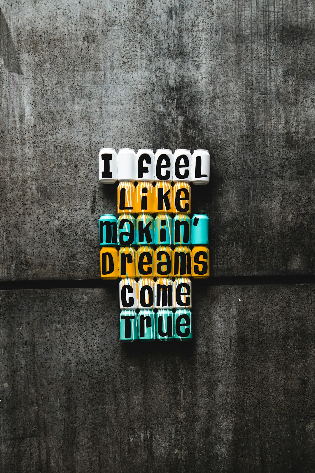 Stacked colorful blocks with the text "I feel like makin’ dreams come true" against a textured concrete wall background.